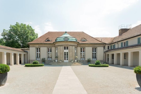 Un grand bâtiment de style classique, doté d’un dôme central, de deux ailes symétriques et d’une cour dallée.