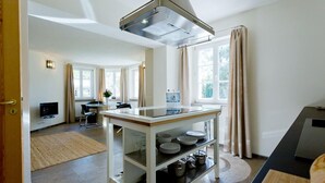 A modern kitchen with a central island, a built-in oven, and a large window with curtains. - Gästehaus am Lehnitzsee (Potsdam)