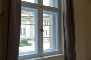 A window with white frames and a view of a building with classical architecture. - Gästehaus am Lehnitzsee (Potsdam)