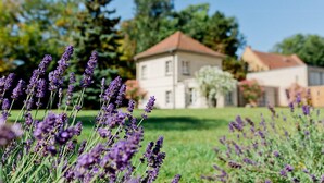 A building with a red roof and a garden with lavender plants in the foreground. - Gästehaus am Lehnitzsee (Potsdam)