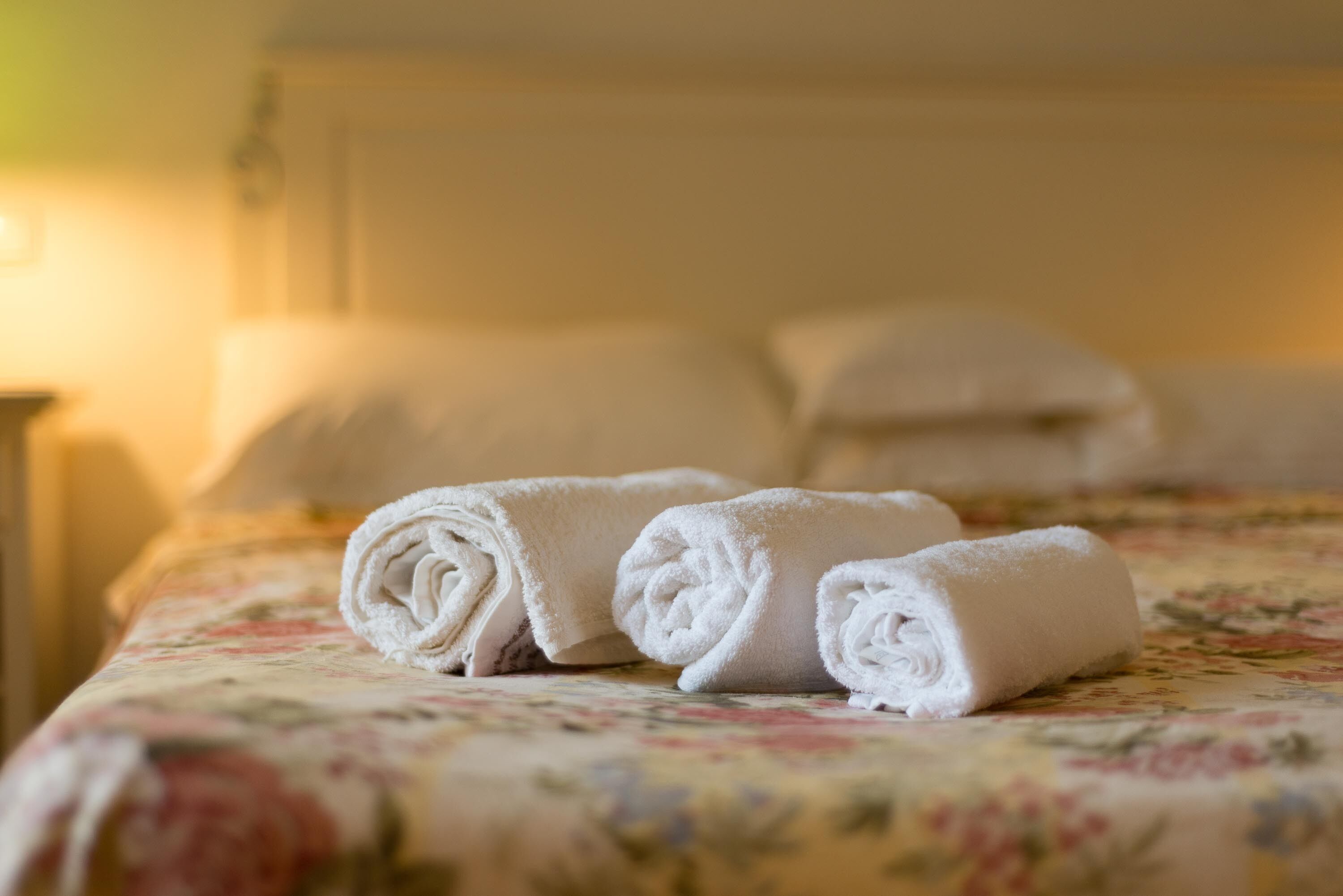 A neatly made bed with rolled white towels and a floral bedspread.