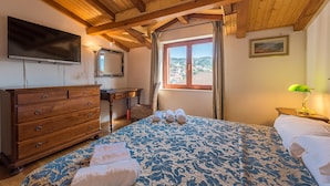 A bedroom with a wooden ceiling, a bed with a patterned bedspread, a dresser, a television, a window with curtains, and a painting on the wall. - Aparthouse - Villa Napoleon (Jelsa)