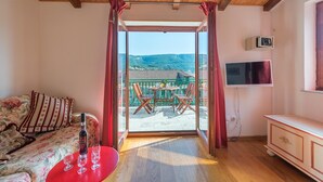 A room with a wooden ceiling, a bed with floral bedding, a red table with glasses, and a balcony with a TV. - Aparthouse - Villa Napoleon (Jelsa)