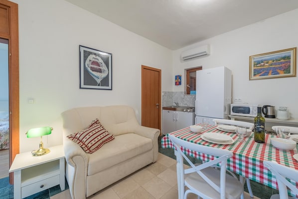 A compact living space with a kitchenette, a dining table set for four, and a sofa with a patterned throw.