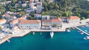Une vue aérienne d’une ville côtière avec un port de plaisance, des bâtiments aux toits recouverts de tuiles rouges et une promenade en bord de mer aux eaux d’un bleu limpide.