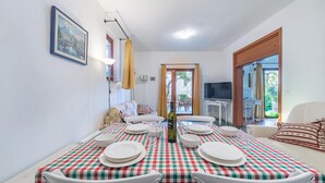 A dining area with a checkered tablecloth, white chairs, and a bottle of wine. There is a framed picture on the wall and a sofa with patterned cushions. - Aparthouse - Villa Napoleon (Jelsa)