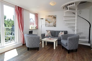 A living room with a grey sofa, two armchairs, a coffee table, a spiral staircase, and a large window with red curtains. - Hüs Lörki 3, Germany (Sylt)