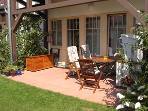 Un espace patio aménagé avec une table en bois, deux chaises, un banc en bois et un fauteuil en osier.