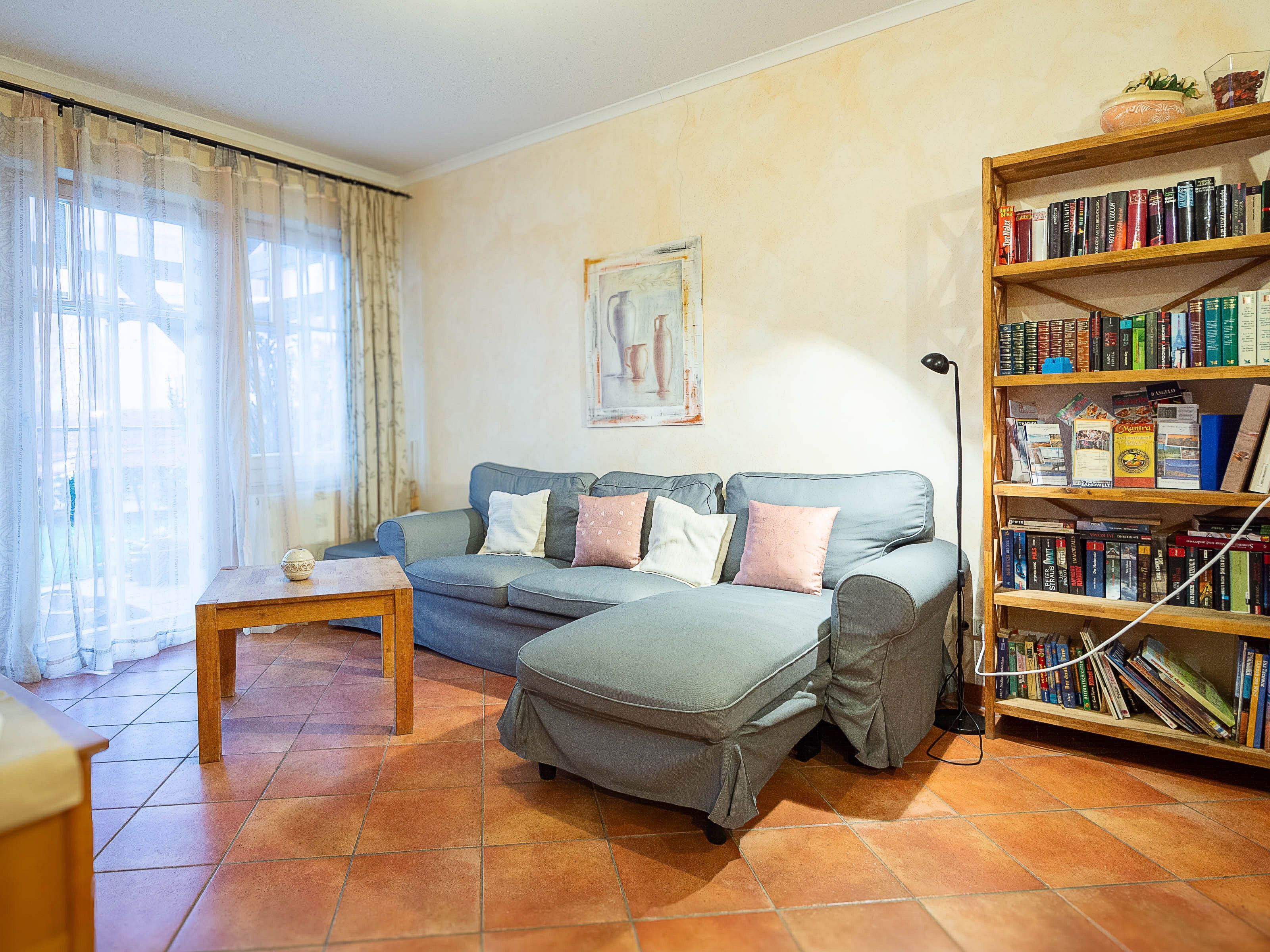 A living room with a sofa, ottoman, and a wooden bookshelf filled with books.