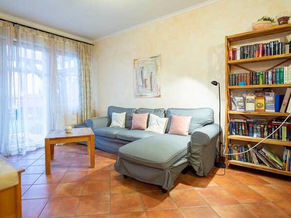 Un salon comprenant un canapé, un pouf et une bibliothèque en bois remplie de livres.