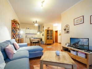 A living room with a sofa, a coffee table, and a television. There is a kitchen in the background with cabinets and a sink. - Residence Seestern Whg S-02. - Lake-02 (Kühlungsborn)