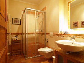 Un baño con ducha envuelta en vidrio, inodoro, lavamanos y toallero con toallas.