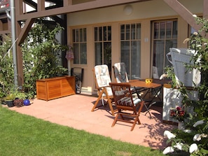 Un patio con una mesa de madera, dos sillas, un banco de madera y una silla de mimbre.