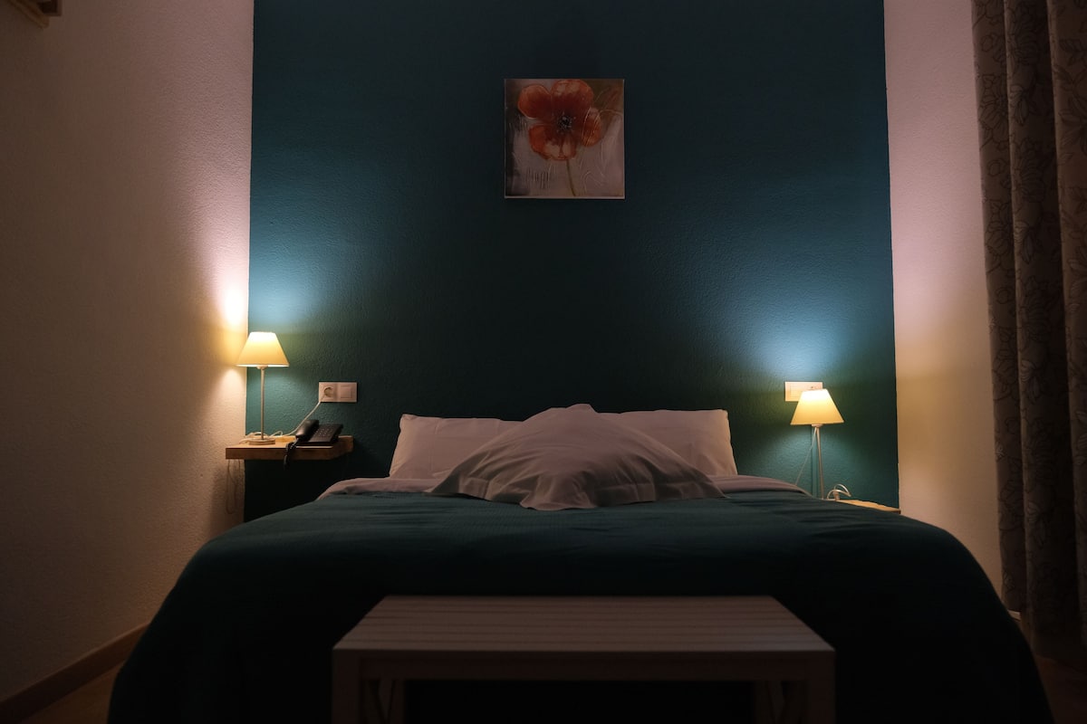A hotel room with a bed, two bedside lamps, a small table, and a wall-mounted painting.
