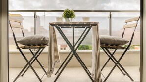 Un balcon avec une table et deux chaises, une petite plante en pot et une vue sur le paysage urbain.