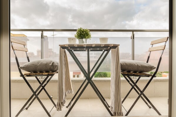Un balcon avec une table et deux chaises, une petite plante en pot et une vue sur le paysage urbain.
