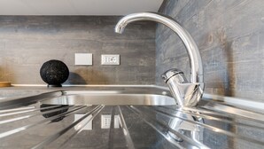 Une cuisine moderne avec un évier en acier inoxydable, un objet sphérique noir posé sur le plan de travail et un pare-feu en bois.