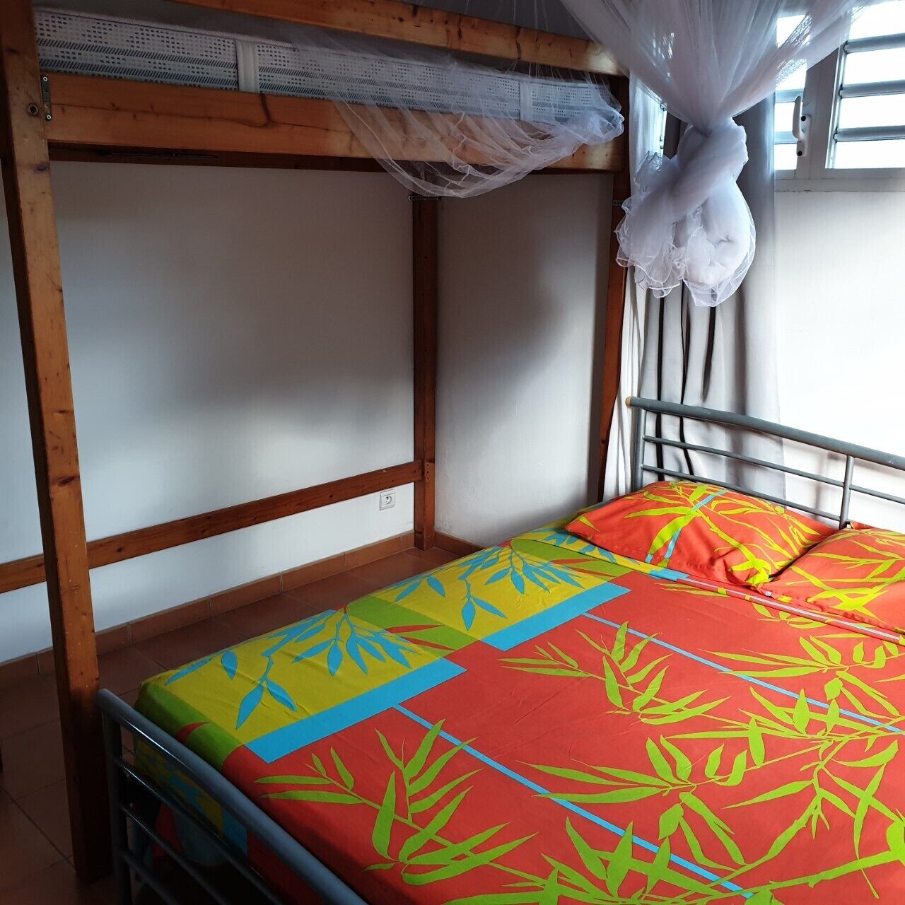 Een stapelbed met een kleurrijke spreideken en een klamboe erboven.