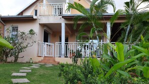 A two-story house with a balcony, a garden with stepping stones, and tropical plants. - VillaRosa Guadeloupe (Sainte-Rose)