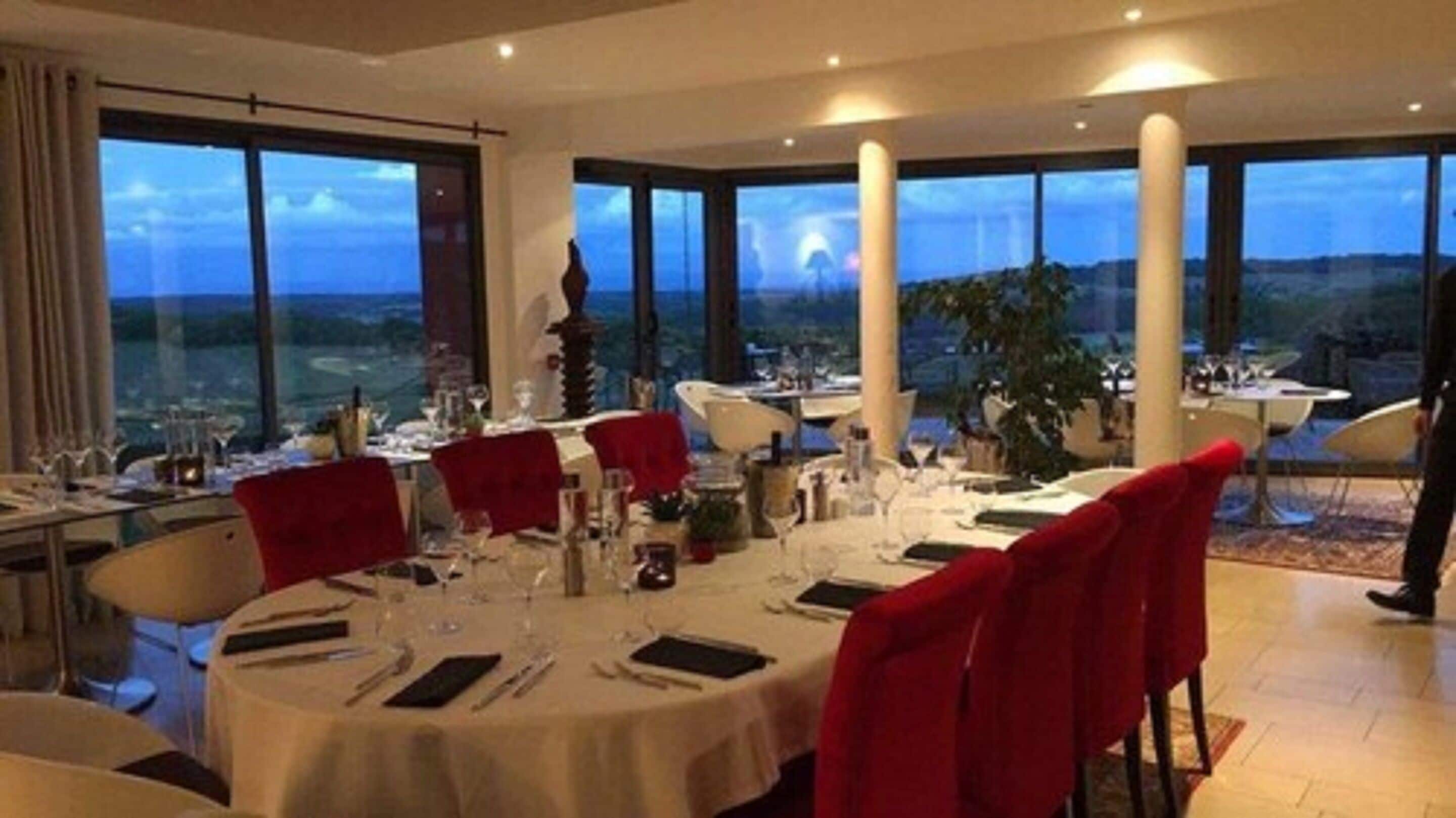 Un comedor con mesas redondas, sillas rojas y vistas del paisaje a través de amplias ventanas.