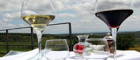 Una mesa con copas de vino y un jarrón con flores, frente a una vista panorámica al aire libre.
