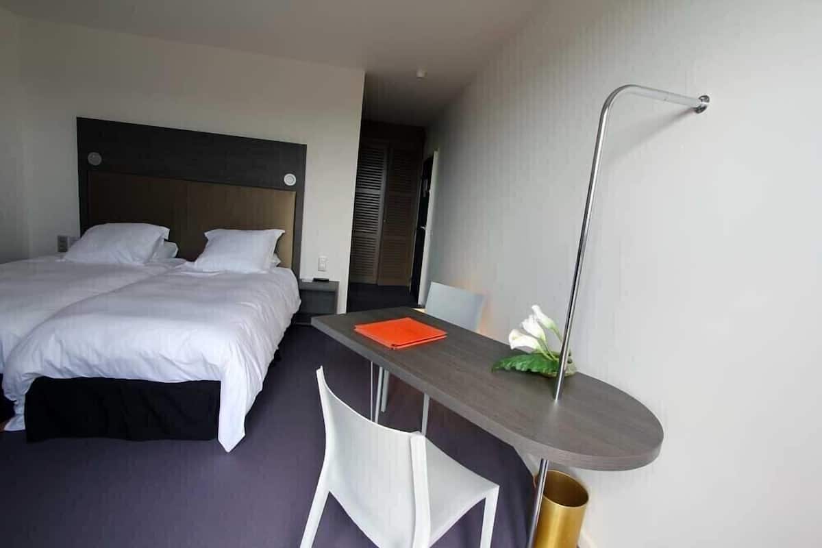 Une chambre d’hôtel avec un lit, un bureau, une chaise et une table de chevet.
