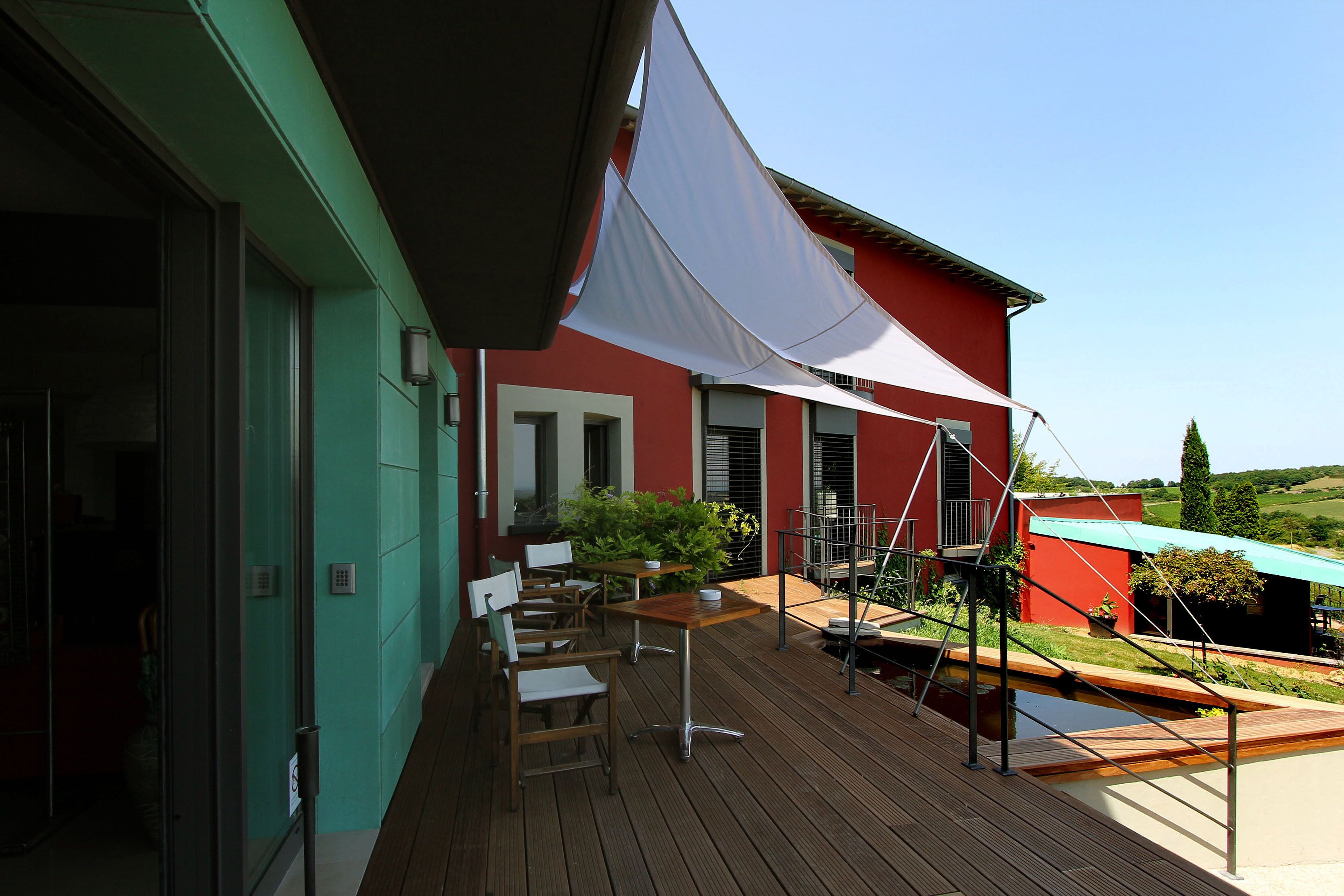 Une terrasse en bois avec des sièges d’extérieur, un auvent blanc et un bâtiment rouge en arrière-plan.