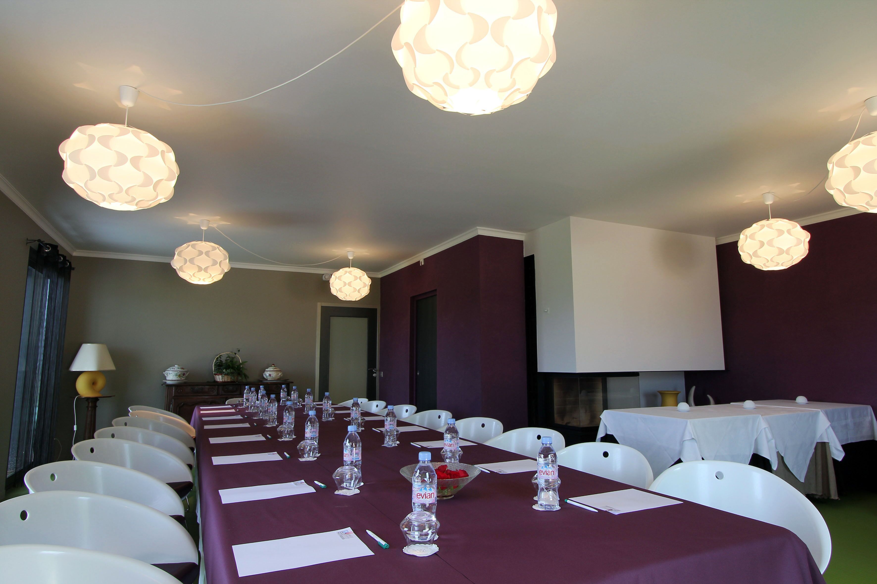 Een vergaderzaal met een lange tafel gedekt voor een vergadering, witte stoelen en decoratieve hanglampen.