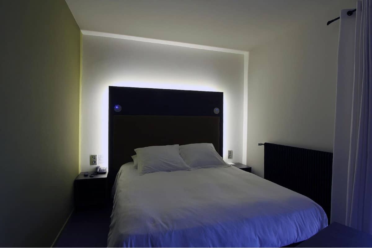 Une chambre d’hôtel dotée d’un grand lit, d’une table de chevet, d’une petite table et d’une tête de lit avec éclairage intégré.