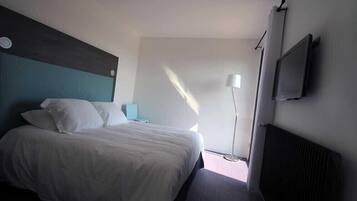 A bedroom with a bed, a nightstand, a lamp, a TV, and a radiator.