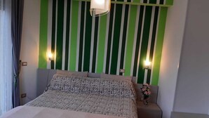 A hotel room with a bed, a nightstand, a lamp, and a wall with vertical stripes. - English Inn rooms (Sorrento)