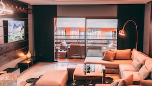 A modern living room with a sofa, coffee table, and TV. There is a balcony with outdoor furniture and a view of a building. - Appart F3 Deluxe Carré Eden (Marrakech)