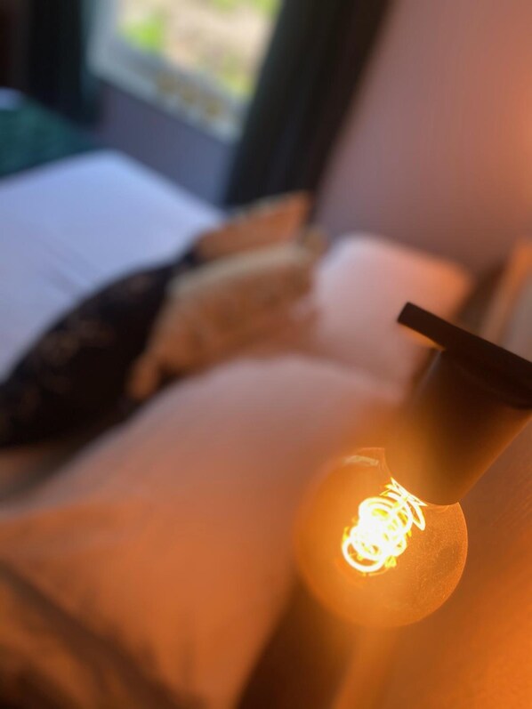Un gros plan d’une ampoule dans une pièce où se trouvent un lit et des oreillers.