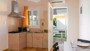 Cocina compacta con estufa, pileta y armarios, que da a un espacio exterior con mesa y sillas.