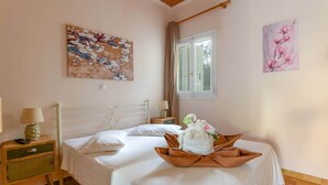 Un dormitorio ordenado con una cama, una mesita de noche con lámpara y dos cuadros colgados en la pared.