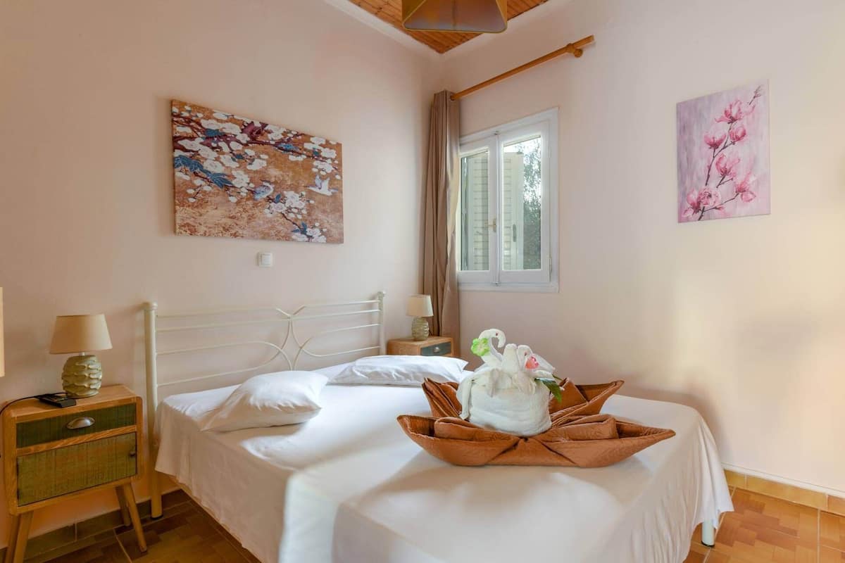 Un dormitorio ordenado con una cama, una mesita de noche con lámpara y dos cuadros colgados en la pared.