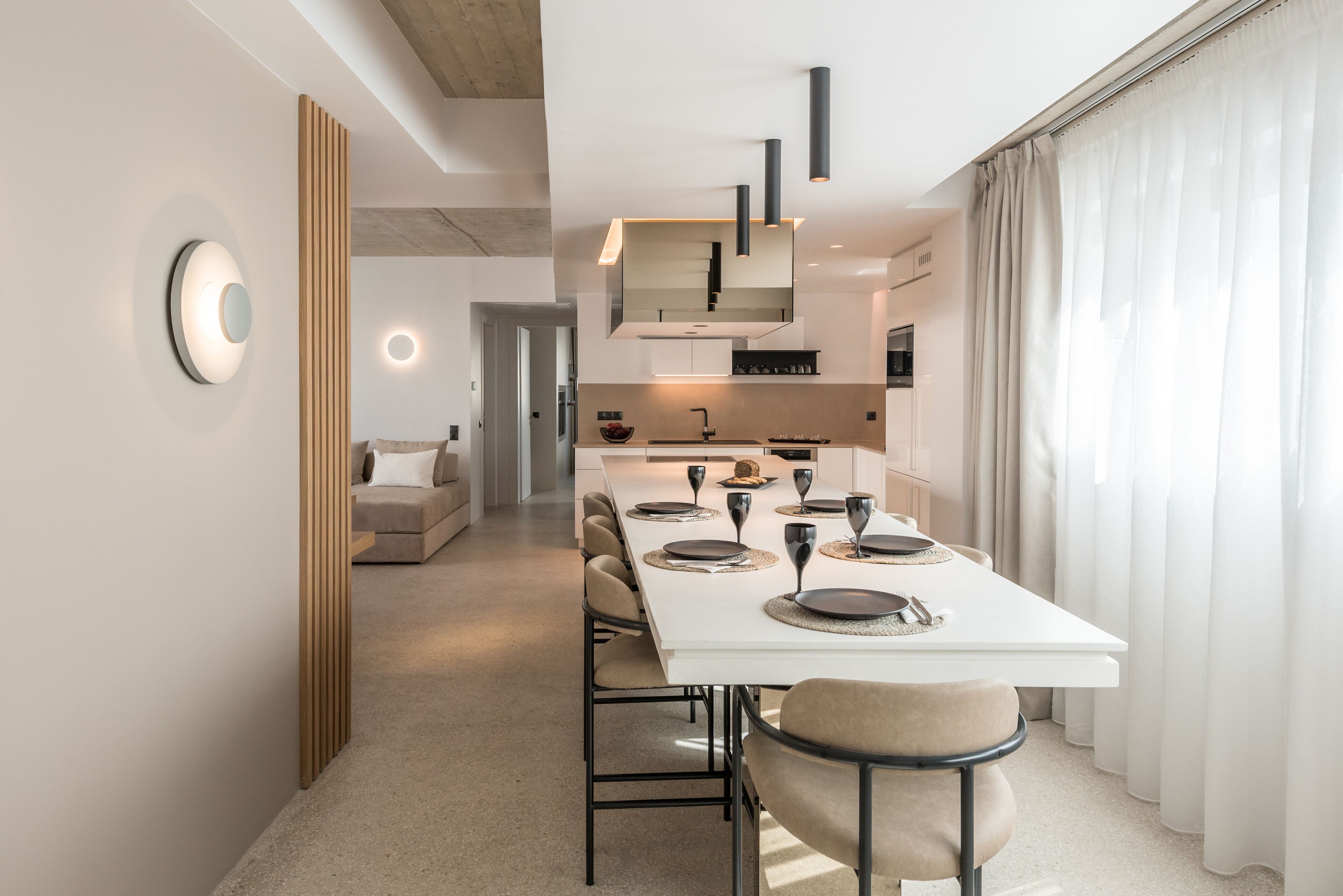 A modern dining area with a long table set for six, a kitchen in the background, and a living area with a sofa and a coffee table.