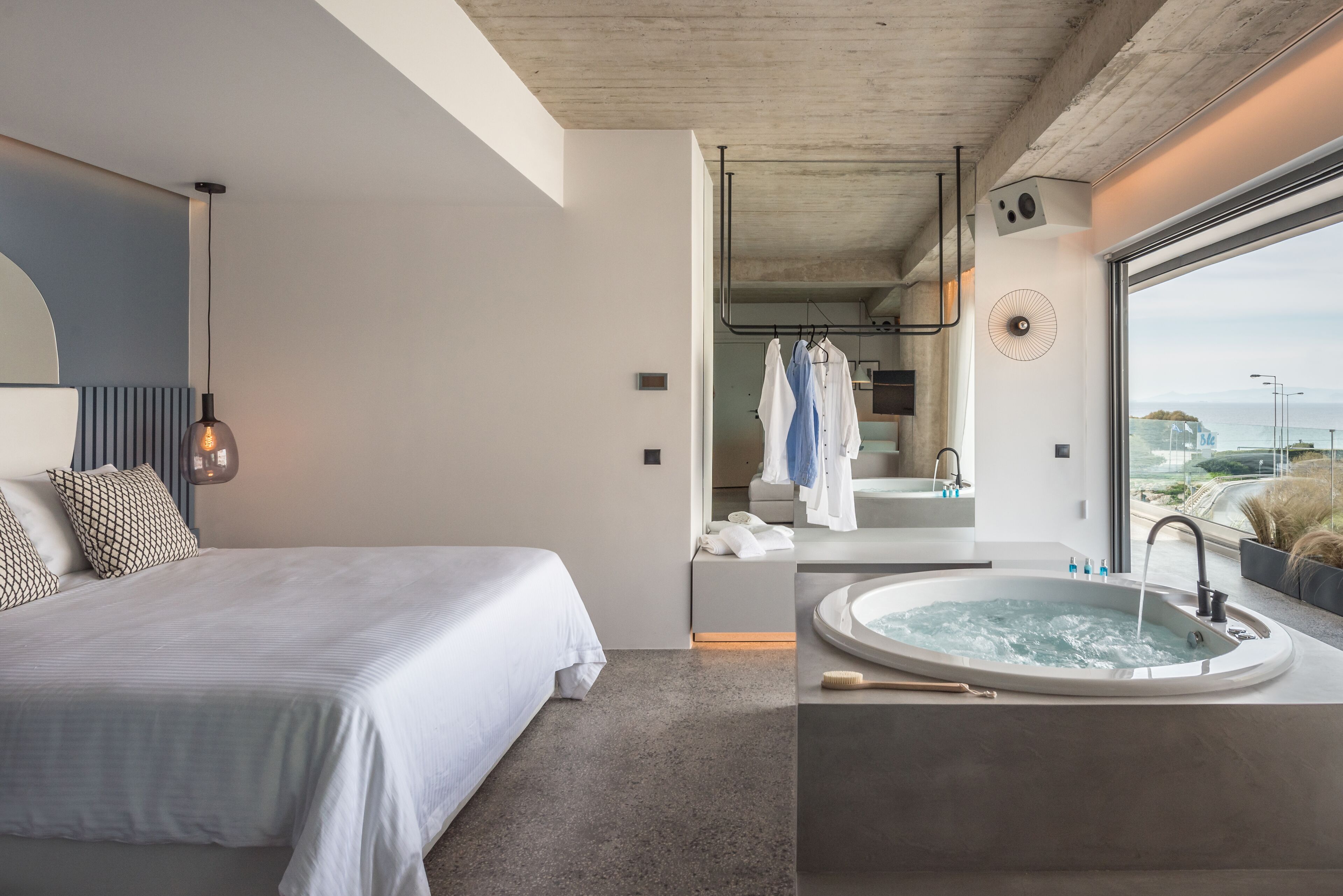 A modern bedroom with a large bed, a bathroom with a bathtub, and a view of the sea.