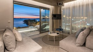 A modern living room with a large sliding glass door leading to a balcony, a flat-screen TV mounted on the wall, and a round coffee table. - Urban Suites (Alimos)