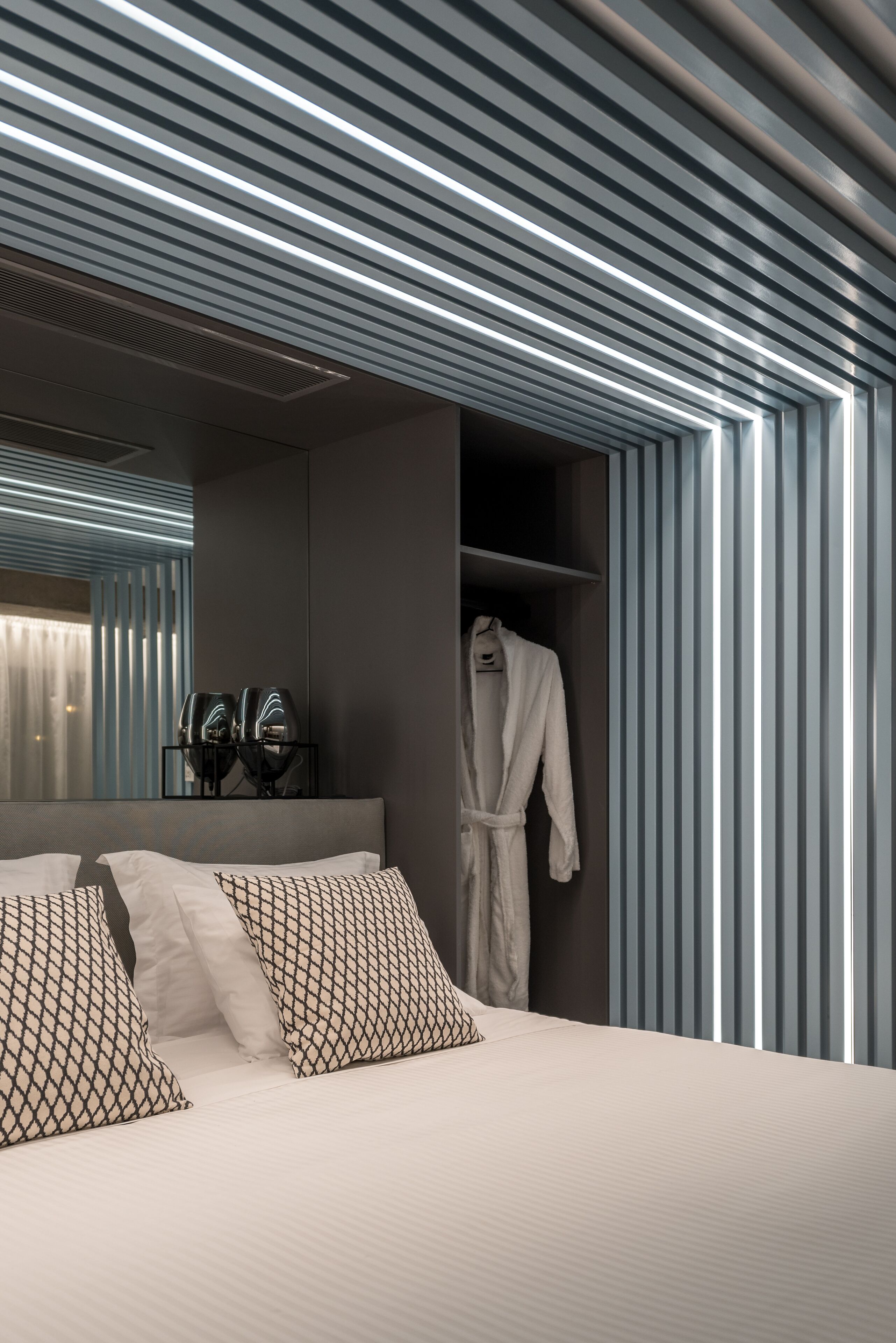 Et moderne hotelværelse med en stor seng, en badekåbe på stativ og et spejl over sengen.