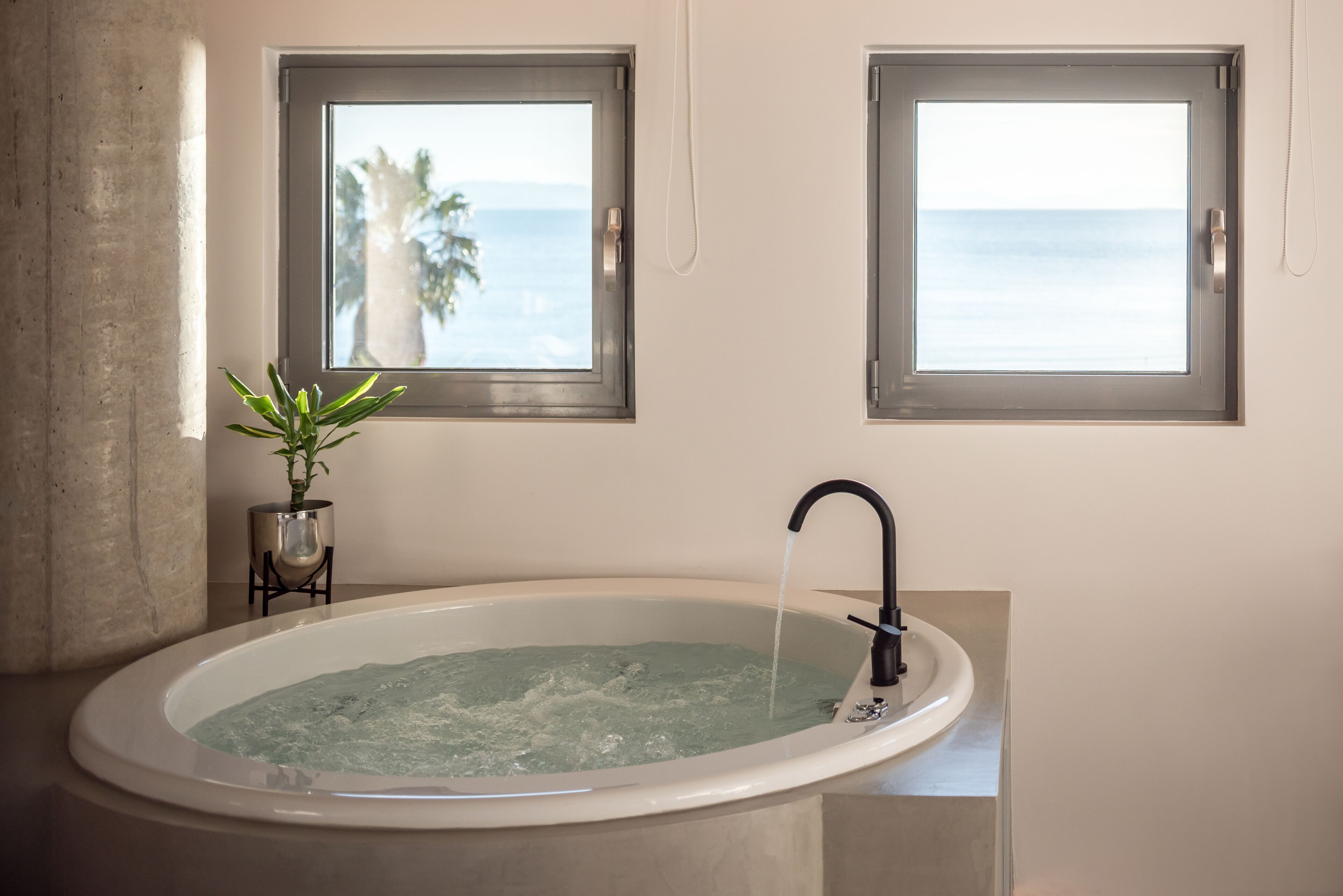 Un baño con una bañera grande, dos ventanas con vistas al océano y una planta en maceta.