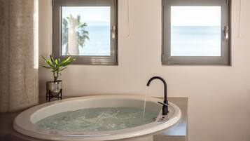 Un baño con una bañera grande, dos ventanas con vistas al océano y una planta en maceta.
