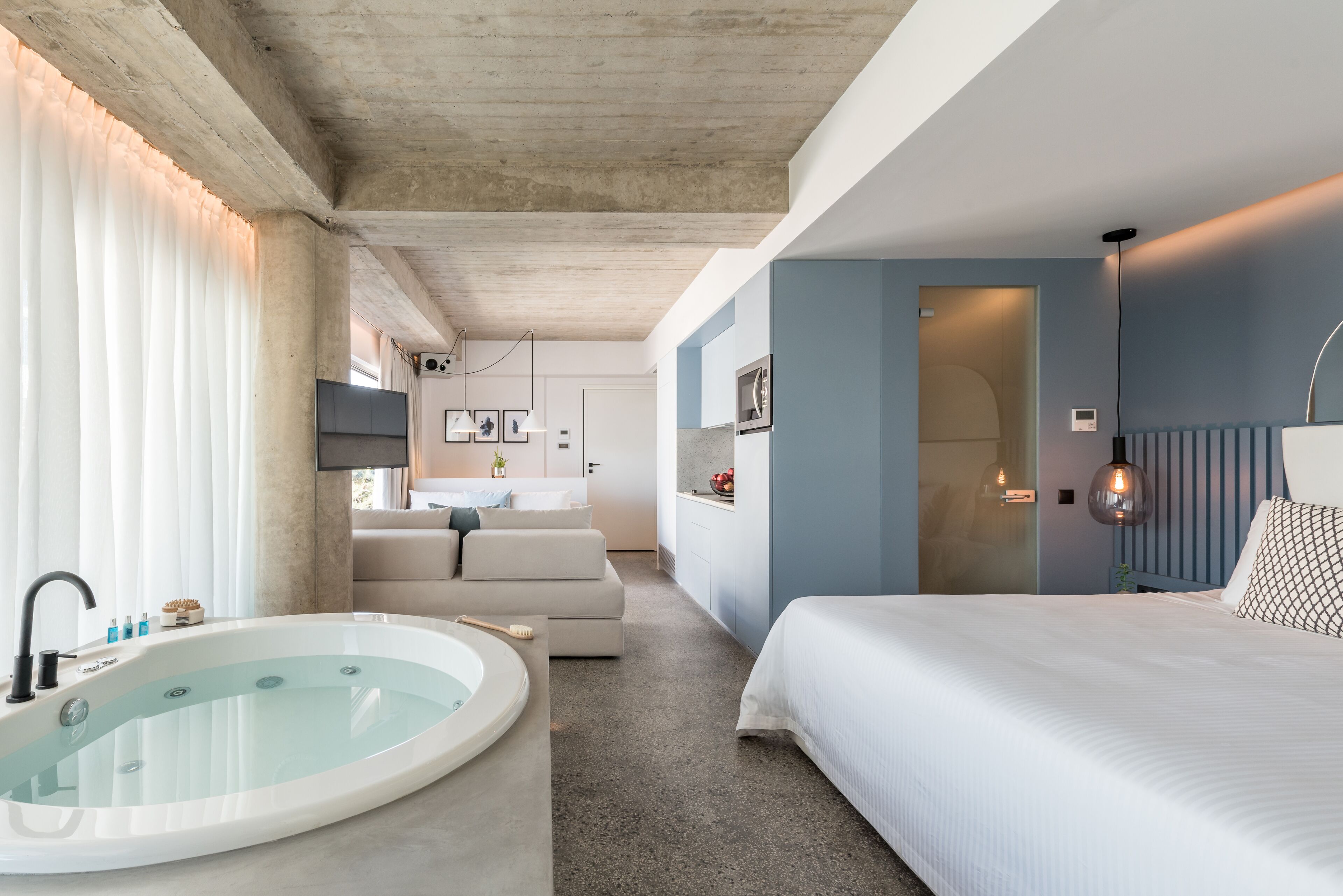 A modern hotel room with a bathtub, a bed, a sofa, and a bathroom with a shower.