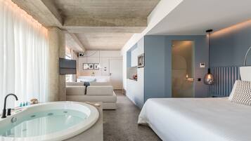 A modern hotel room with a bathtub, a bed, a sofa, and a bathroom with a shower.