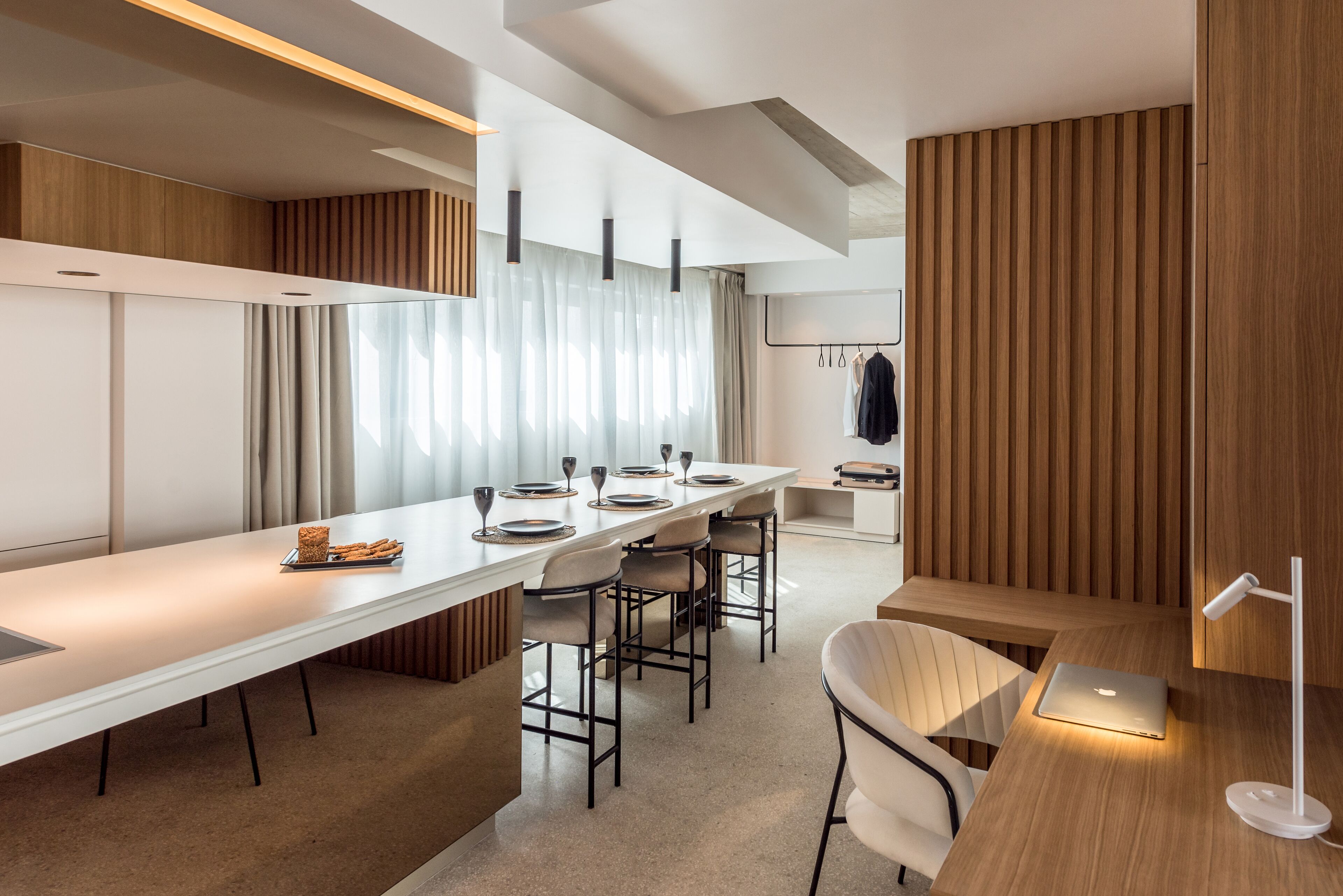 A modern kitchen with a long countertop, bar stools, and a laptop on the table.