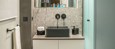 A modern bathroom with a rectangular sink, two black faucets, a potted plant, and a mirror above the sink.