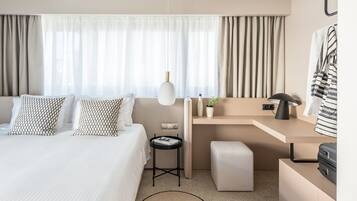 A modern hotel room with a bed, bedside table, desk, and a small seating area.