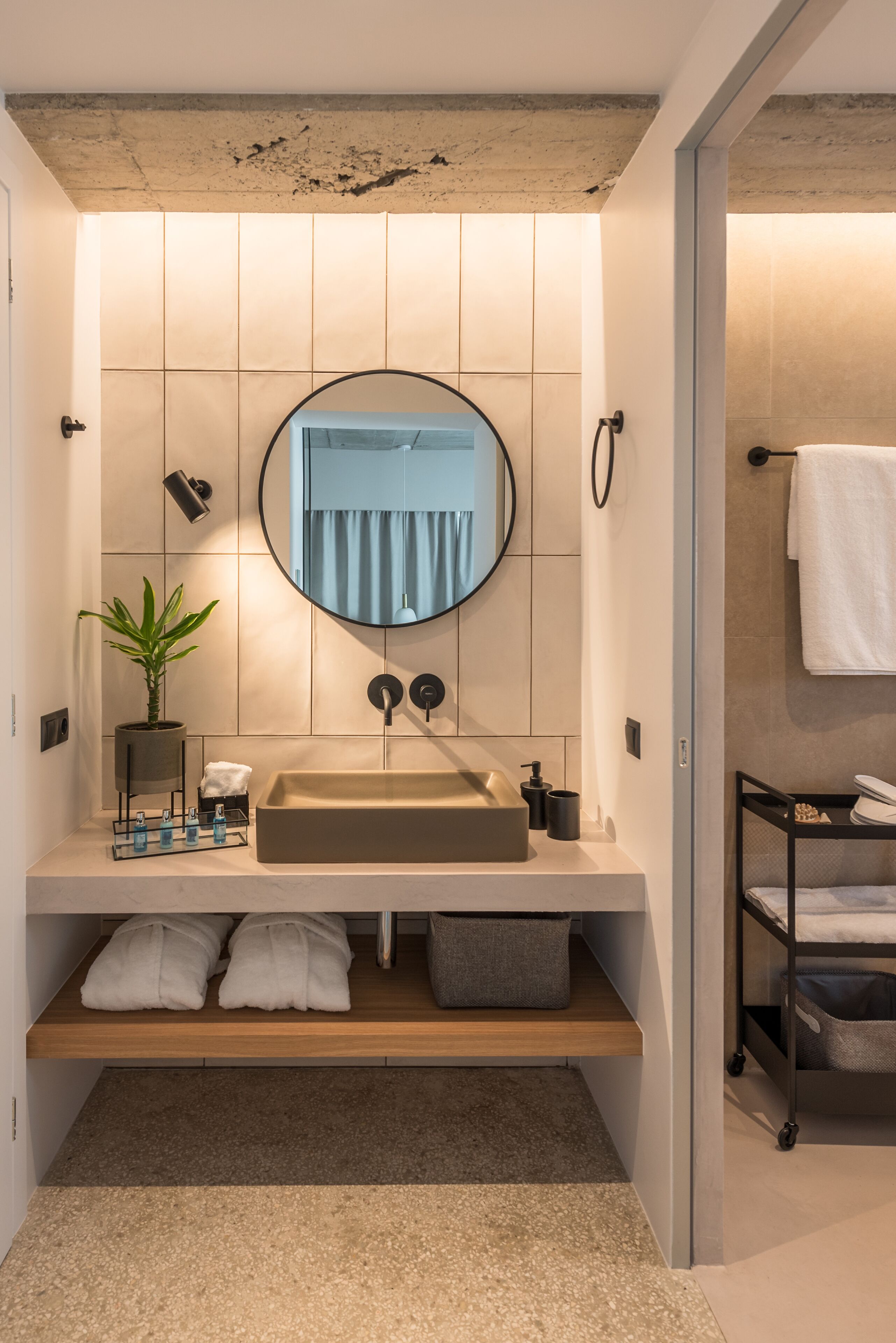 Un bany modern amb un mirall rodó gran, un lavabo beix i una prestatgeria de fusta.