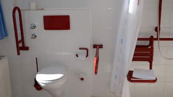 A bathroom with a toilet, a red grab bar, a white shower curtain, and a towel rack.