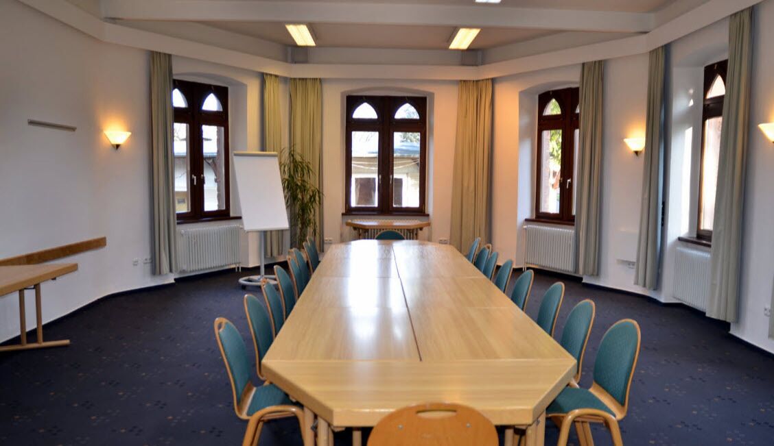 A conference room with a long table, chairs, a whiteboard, and windows with curtains.